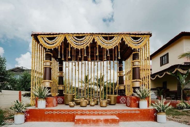 Outdoor mandap with bamboo and gold pillars, marigold garlands and red carpet steps by RAW Group